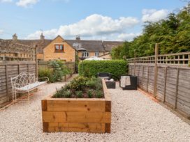 A garden with a wooden planter box gravel flooring a metal bench and outdoor seating at Puffitts Cottage in Bourton-on-the-Water