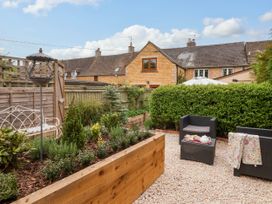 A garden with a raised wooden planter a white metal bench and black wicker chairs with a table at Puffitts Cottage in Bourton-on-the-Water