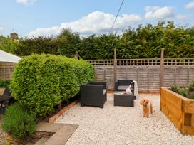 A backyard seating area with black wicker chairs and table on gravel near wooden planter and green bushes at Puffitts Cottage in Bourton-on-the-Water