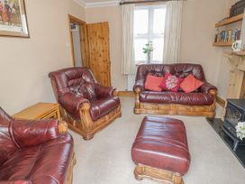 A living room with leather armchairs a leather sofa cushions a wooden door and a window with curtains at Jasmine Cottage in Rhuddlan