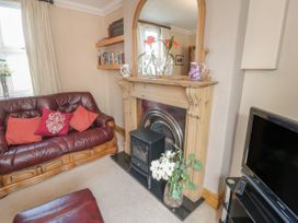 A living room with a leather sofa red cushions fireplace with mirror bookshelves and a television at Jasmine Cottage in Rhuddlan