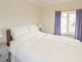 A bedroom with a double bed white bedding bedside tables lamps and a window with purple curtains at Jasmine Cottage in Rhuddlan