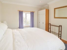 A bedroom with a bed white bedding a window with purple curtains a white wardrobe a mirror on the wall and a wooden towel rack at Jasmine Cottage in Rhuddlan