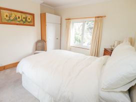 A bedroom with a bed a wardrobe a chair a window with curtains and a painting at Jasmine Cottage in Rhuddlan