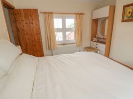 A bedroom with a white bed next to a wooden door a window with curtains and a dresser with a round mirror at Jasmine Cottage in Rhuddlan
