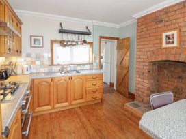 A kitchen with wooden cabinets a stove a double sink hanging pots a brick fireplace and a wooden door at Jasmine Cottage in Rhuddlan