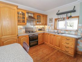 A kitchen with wooden cabinets a stove and oven a double sink and hanging pots at Jasmine Cottage in Rhuddlan
