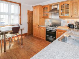 A kitchen with wooden cabinets a gas stove a stainless steel sink a table with chairs and a window with vertical blinds at Jasmine Cottage in Rhuddlan