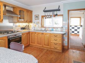A kitchen with wooden cabinets a stove a sink pots hanging above the window and a door leading to a laundry room at Jasmine Cottage in Rhuddlan