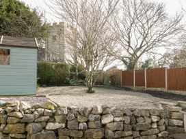 A garden with a stone wall a shed trees and a church tower in the background at Jasmine Cottage in Rhuddlan