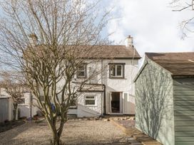 A backyard with a tree a small shed and a white two story house with open doors at Jasmine Cottage in Rhuddlan
