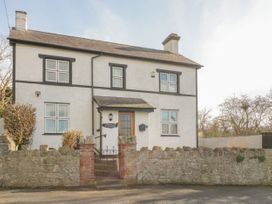 The exterior of a two-story house with white walls and black trim behind a stone wall and gate at Jasmine Cottage in Rhuddlan