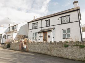 A white two-story house with black window frames and a stone wall with a gate in front at Jasmine Cottage in Rhuddlan