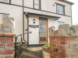 The exterior of a two-story house with a wooden door, stone and brick walls, a black metal gate, and a sign that says Jasmine Cottage in Rhuddlan