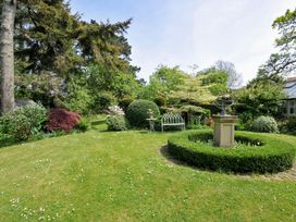 A garden with trees, bushes, and a sundial at The Coach House at Pendower House Fowey