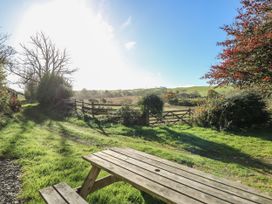 A wooden picnic table on grass near a dirt path with a wooden gate and fields in the background at Pengraig near Tregaron