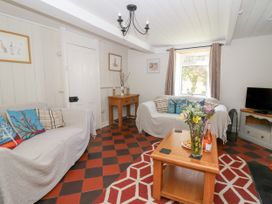 A living room with two sofas with cushions a wooden coffee table with flowers and a bottle a small wooden side table and a television near a window at Pengraig near Tregaron