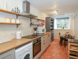 A kitchen with wooden countertops, shelving with jars and glasses, an oven, microwave, washing machine, and a dining table near a window at Pengraig near Tregaron