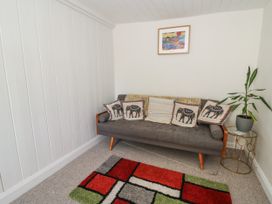 A room with a gray sofa with elephant patterned cushions a side table with a plant and a colorful rug on the floor at Pengraig near Tregaron
