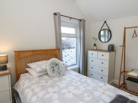 A bedroom with a bed a dresser a round mirror a wooden garment rack and a window with curtains at Pengraig near Tregaron