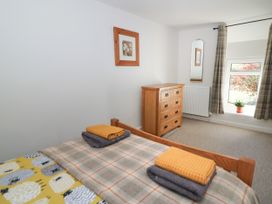 A bedroom with a wooden bed, a chest of drawers, a window with curtains, a mirror, and a framed picture on the wall at Pengraig near Tregaron