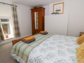 A bedroom with a bed, folded towels, a wooden wardrobe, a window with curtains, and a framed picture at Pengraig near Tregaron