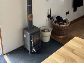 A wood stove with a chimney and a basket of firewood at Shepherds Cabin at Titterstone Clee Hill