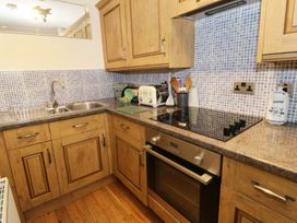 A kitchen with wooden cabinets double sink electric stove and oven with blue tiled backsplash at Gelli Glud in Eglwysbach