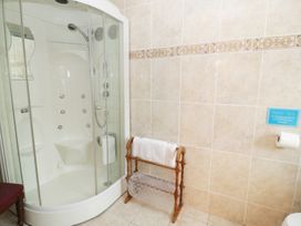 A bathroom with a curved glass shower enclosure a wooden towel rack and tiled walls at Gelli Glud in Eglwysbach
