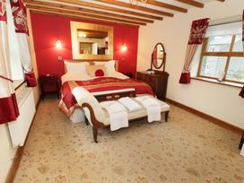 A bedroom with a double bed bench at the foot of the bed carpeted floor and wooden furniture at Gelli Glud in Eglwysbach