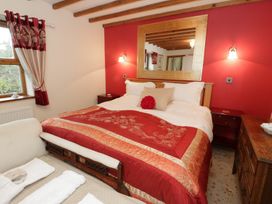 A bedroom with a bed covered in red and gold bedding a wooden dresser and an armchair at Gelli Glud in Eglwysbach