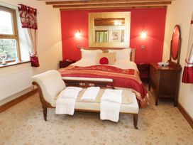 A bedroom with a double bed red and beige bedding a bench with towels a dresser and red curtains at Gelli Glud in Eglwysbach
