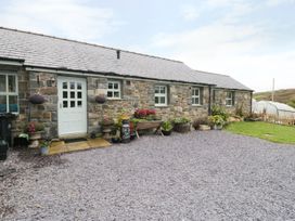 A stone building with a white door and windows surrounded by potted plants and a gravel courtyard at Gelli Glud in Eglwysbach