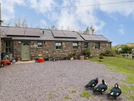 An outdoor view of a stone house with solar panels and ducks at Gelli Glud Eglwysbach