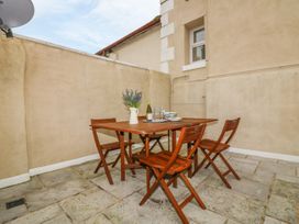An outdoor patio with a wooden table and four chairs and a vase with flowers at Cottage 1 Newcourt in Torquay