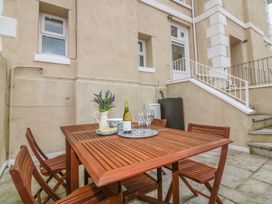 An outdoor patio with a wooden table and chairs a bottle of wine glasses and flowers at Cottage 1 Newcourt Torquay