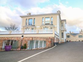 A large beige multi-story building with white balcony railings and stone lower walls with an empty asphalt driveway at Cottage 1 Newcourt in Torquay