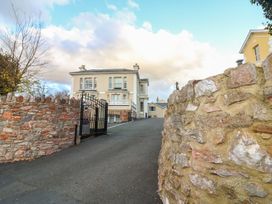 A driveway with a black gate leading to a beige house with multiple windows and stone walls on both sides at Cottage 1 Newcourt in Torquay