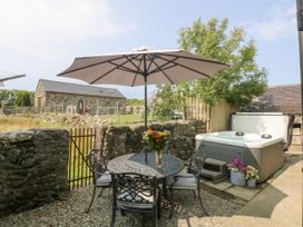 An outdoor area with a table and chairs under a parasol and a hot tub at Cegin Foch in Chwilog