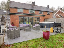 A backyard patio with wicker seating and purple cushions a hot tub a barbecue grill and a red planter at Hiraeth in Cwmtaf near Cefn-Coed-Y-Cymmer