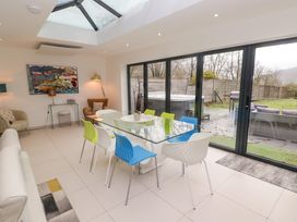 A dining area with a glass table and colorful chairs next to large sliding glass doors opening to a garden at Hiraeth in Cwmtaf near Cefn-Coed-Y-Cymmer