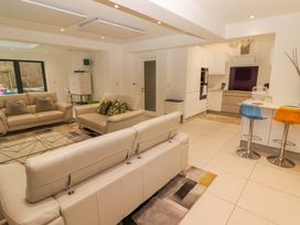 A living room with beige sofas and a glass coffee table next to a kitchen with a breakfast bar and colorful stools at Hiraeth in Cwmtaf near Cefn-Coed-Y-Cymmer