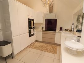 A kitchen with white cabinets beige drawers a stove with a purple backsplash and a sink with a black faucet at Hiraeth in Cwmtaf near Cefn-Coed-Y-Cymmer