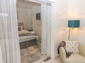 A bedroom with a bed a bedside table and a painting behind glass sliding doors and a corner with a chair a lamp and a cushion at Hiraeth in Cwmtaf near Cefn-Coed-Y-Cymmer