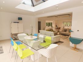 A dining area with a glass table and colorful chairs next to a living room with sofas at Hiraeth in Cwmtaf near Cefn-Coed-Y-Cymmer