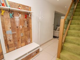 A hallway with a wooden coat rack with colorful hooks a white standing coat rack tiled floor green carpeted stairs and a view into a living room at Hiraeth in Cwmtaf near Cefn-Coed-Y-Cymmer