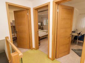 A hallway with three wooden doors leading to a bedroom with bunk beds a bedroom with a double bed and a room with a desk and blue chair at Hiraeth in Cwmtaf near Cefn-Coed-Y-Cymmer