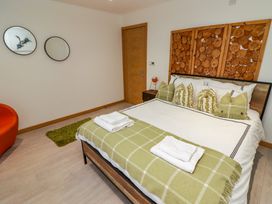 A bedroom with a bed with green pillows and a green blanket two mirrors on the wall an orange chair and a wooden door at Hiraeth in Cwmtaf near Cefn-Coed-Y-Cymmer