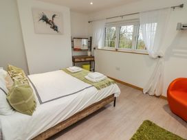 A bedroom with a bed with pillows towels and a green throw a window with white curtains a wooden vanity and an orange chair at Hiraeth in Cwmtaf near Cefn-Coed-Y-Cymmer