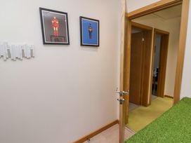 A hallway with two framed pictures of superheroes on the wall and three wooden doors with one open showing a green carpet at Hiraeth in Cwmtaf near Cefn-Coed-Y-Cymmer